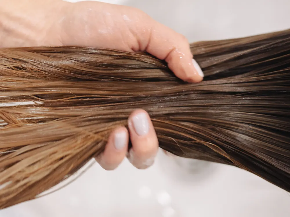 Due mani distribuiscono il trattamento su una ciocca bagnata